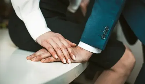 Female and male hands together. Close up shot. Passionate affair at office workplace. Woman wearing skirt sits at edge of office table. Man stands close to her. High quality photo.