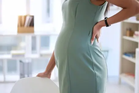 Pregnant, back pain and woman in office and standing for relief, stretching and comfort by chair. Maternity, corporate and female person with ache, pressure and discomfort in workplace and hurt
