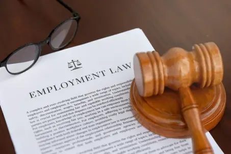 A professional setup featuring an employment law document, a judge's hammer, and glasses on an office table, representing employee rights and labor regulations.