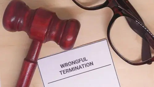 A legal scene displays a gavel, glasses, and wrongful termination documents atop a light surface.